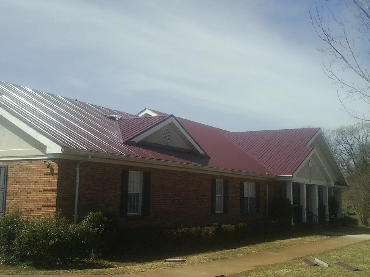 Red metal roof with gabled entries on a long brick building, from a Hail Damage Roof Repair job in Ulysses