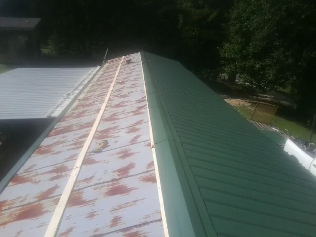 Old rusted panels beside newly installed green metal roofing — Wind Damage Roof Repair by Roofing Brothers in Ulysses