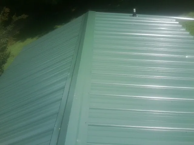 New green metal panels meeting at the ridge of a roof — Flat Roof Repair work by our crew in Ulysses