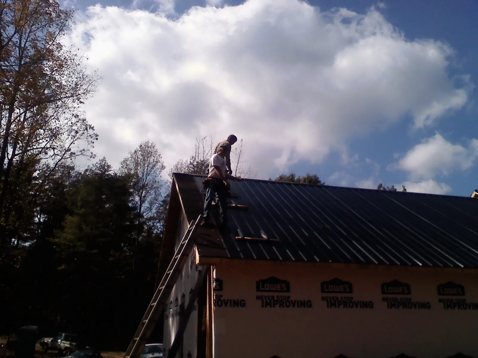 Roofer fastening dark metal panels high against a cloudy sky, from a Roof Inspection job in Ulysses