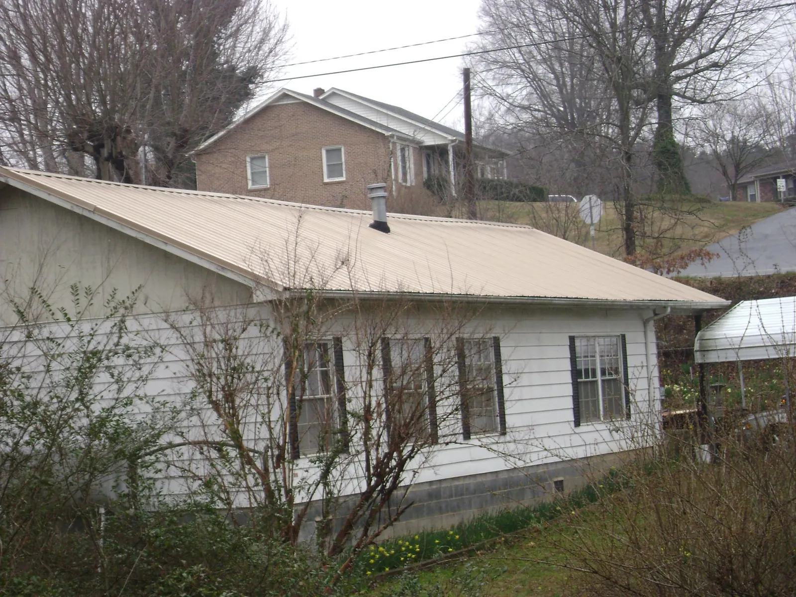 Tan metal roof on a white sided house set into a hillside — Commercial Roofing by Roofing Brothers in Ulysses