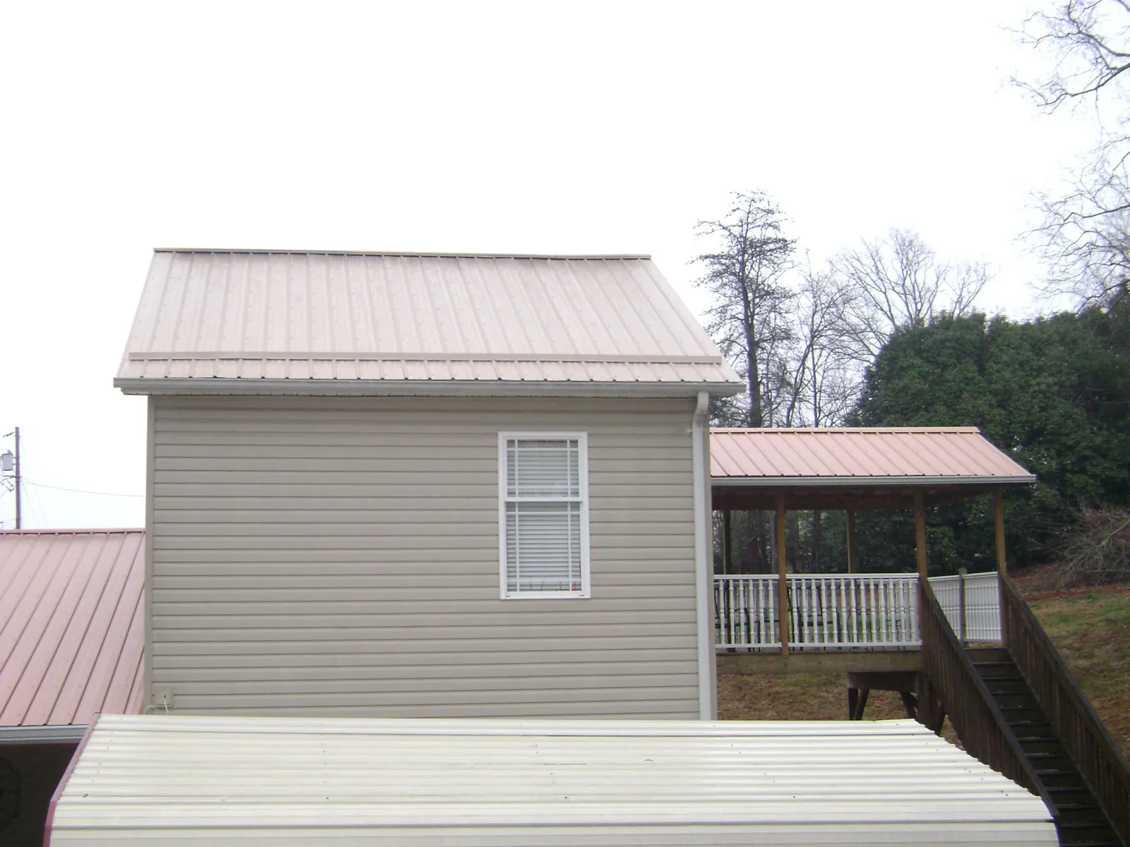 Tan metal roofs on a two story addition and attached porch, from a Roof Replacement job in Ulysses